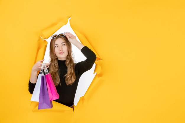 Young fashion woman with shopping bags through torn paper hole in the wall