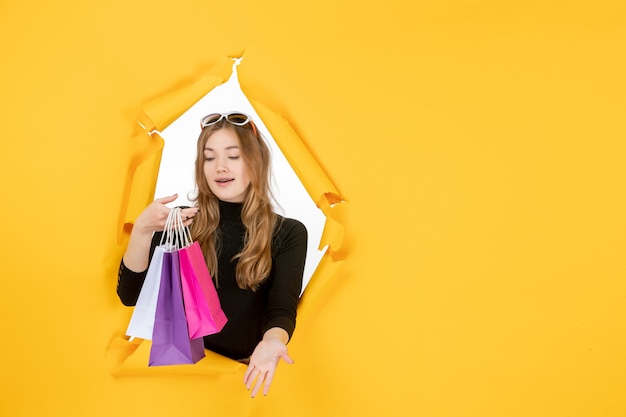 Free photo young fashion woman with shopping bags through torn paper hole in the wall