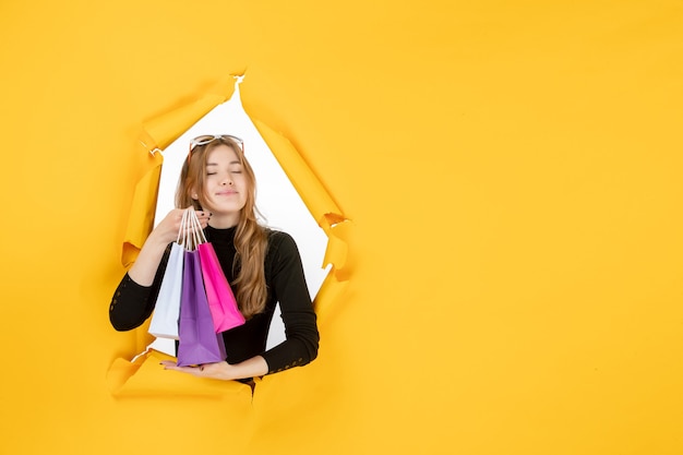 Free photo young fashion woman with shopping bags through torn paper hole in the wall