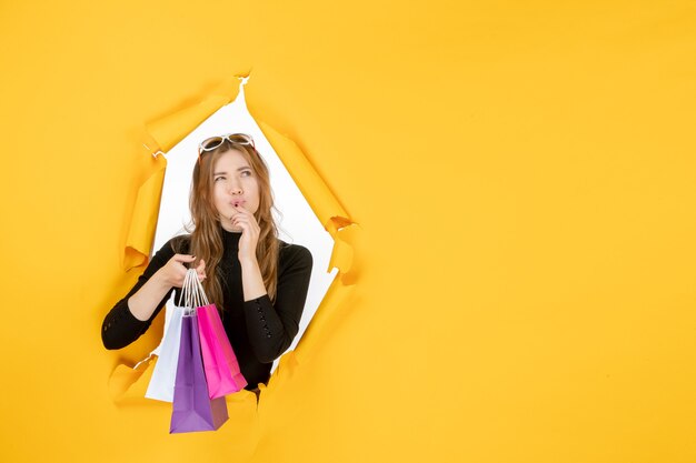 Free photo young fashion woman with shopping bags through torn paper hole in the wall