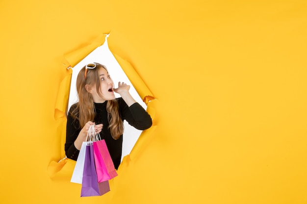 Young fashion woman with shopping bags through torn paper hole in the wall