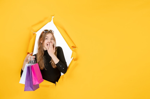 Young fashion woman with shopping bags through torn paper hole in the wall