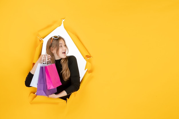 Free Photo young fashion woman with shopping bags through torn paper hole in the wall