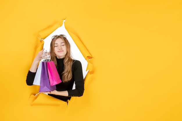 Free photo young fashion woman with shopping bags through torn paper hole in the wall