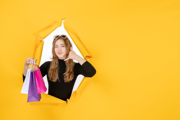 Young fashion woman with shopping bags through torn paper hole in the wall