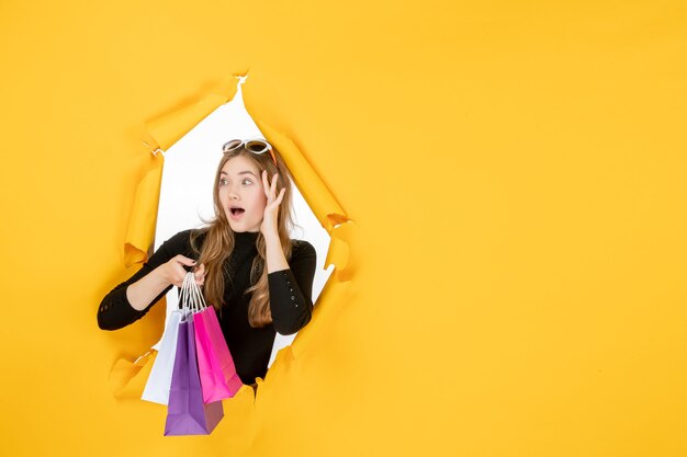 Young fashion woman with shopping bags through torn paper hole in the wall