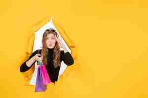 Free photo young fashion woman with shopping bags through torn paper hole in the wall