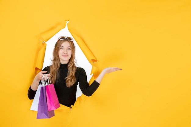 Young fashion woman with shopping bags through torn paper hole in the wall