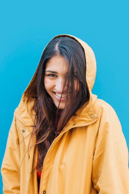 Free photo young fashionable woman wearing yellow hoodie in front of blue backdrop