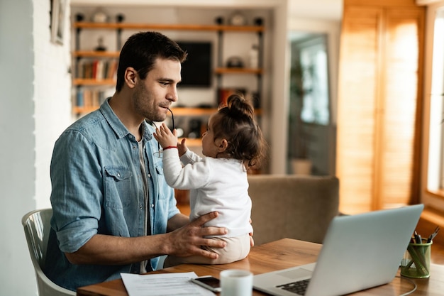 Young father having fun with his baby daughter while working at home