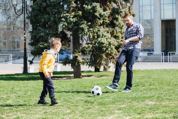 Free photo young father and his son playing football in a park