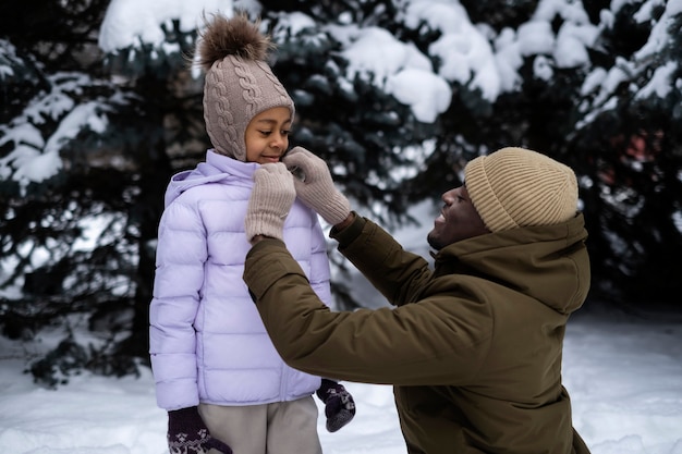 Young father tying his daughter's jacked on a snowy winter day