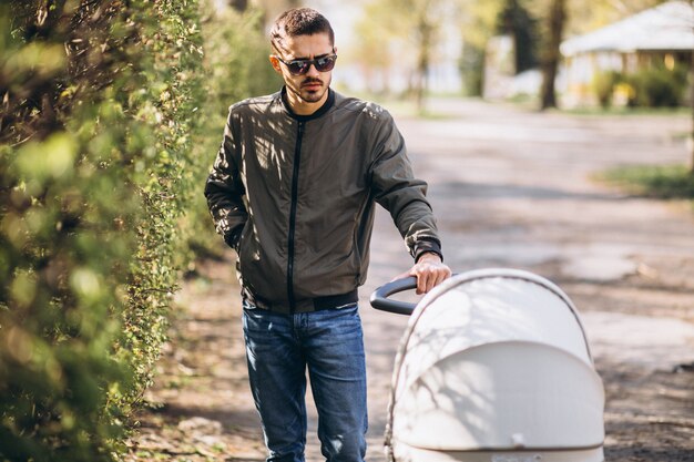 Young father walking with baby carriage in the park