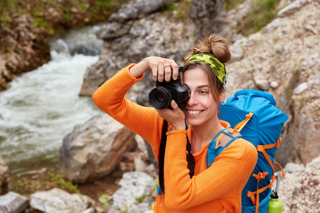 Free photo young female adventurer poses against small river in ravine, holds camera