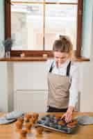 Free photo young female baker removing the muffins from the cupcake mold tray