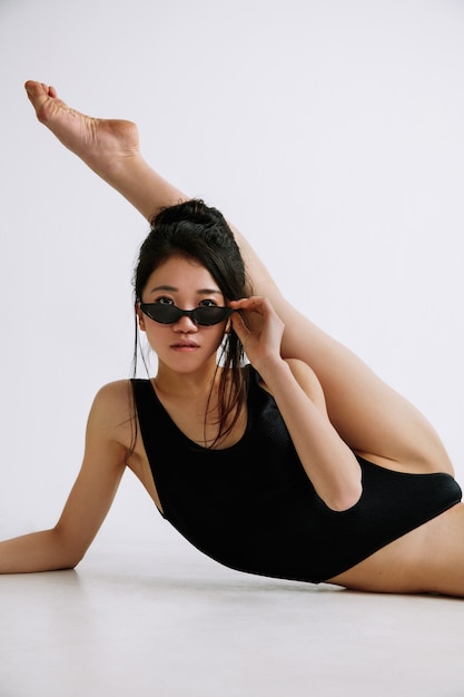 Young female ballet dancer in black bodysuit against white studio wall