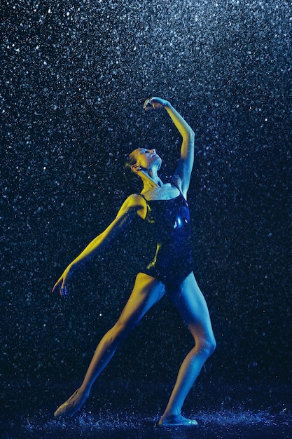 Free photo young female ballet dancer performing under water drops and spray. caucasian model dancing in neon lights. attractive woman. ballet and contemporary choreography concept. creative art photo.