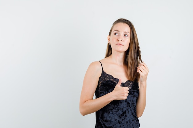 Young female in black singlet showing thumb up while looking away and looking focused