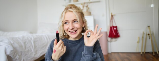 Young female blogger content creator showing lipstick and okay hand sign recommending beauty product