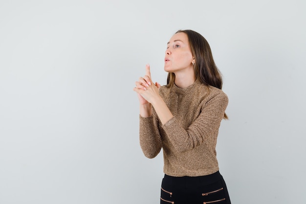 Young female in blouse,skirt showing pistol gesture and looking confident , front view. space for text