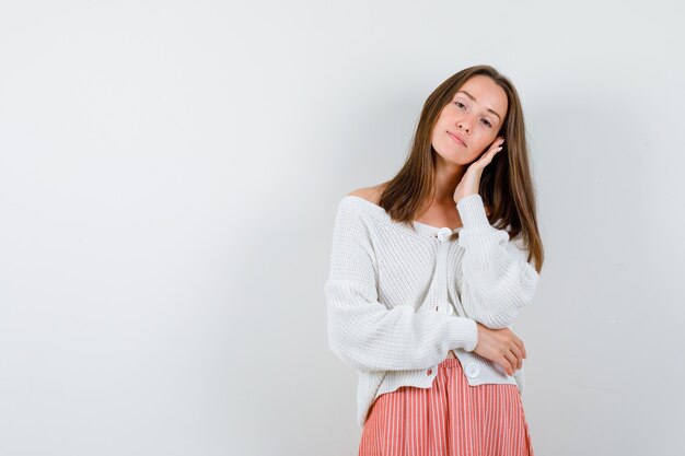 Young female in cardigan and skirt leaning cheek on palm looking sensible isolated