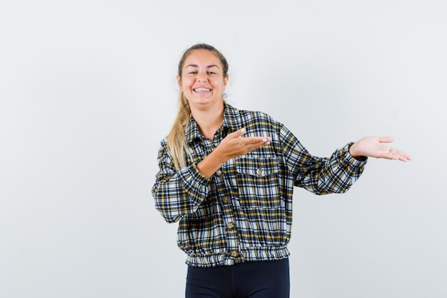 Young female in checked shirt showing something and looking happy , front view.