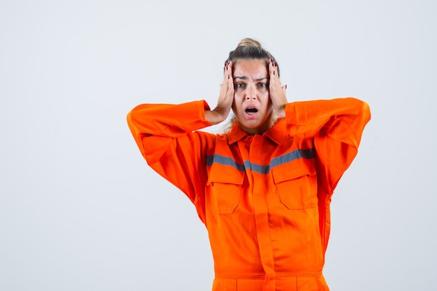 Free Photo young female clasping head with hands in worker uniform and looking perplexed , front view.