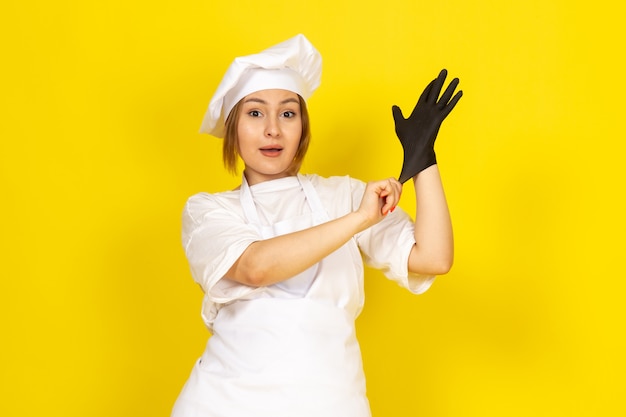 young female cooking in white cook suit and white cap wearing black glove