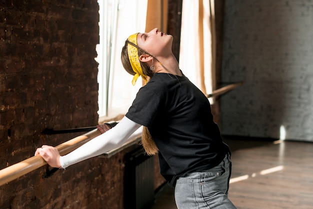 Young female dancer stretching her hands on barre