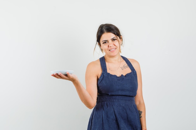 Young female in dark blue dress holding empty saucer and looking jolly