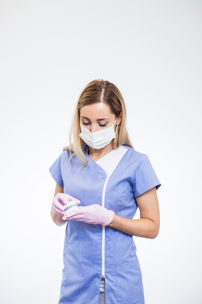 Young female dentist holding teeth model on white backdrop