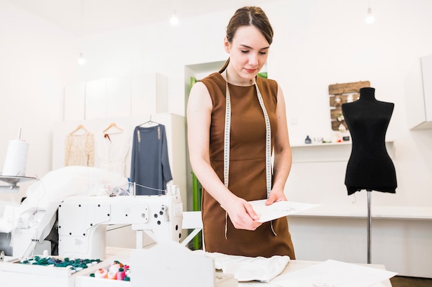 Free photo young female designer holding fashion sketch in shop