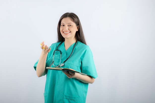 young female doctor standing with notebook and pencil. 