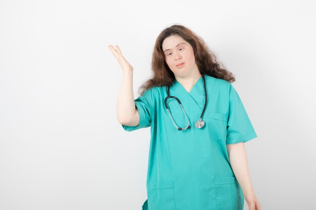 Young female doctor with down syndrome standing on white.