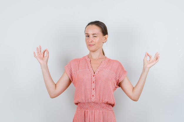 Free photo young female doing meditation and winking eye in striped dress front view.