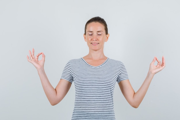 Free photo young female doing meditation with closed eyes in striped t-shirt and looking peaceful. front view.