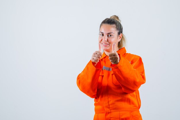 Young female doing positive gesture with hands in worker uniform and looking successful , front view.