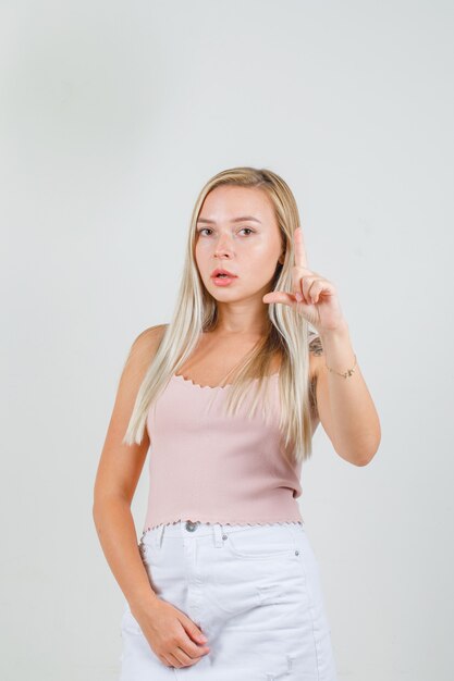 Young female doing small size sign in singlet, mini skirt and looking serious 