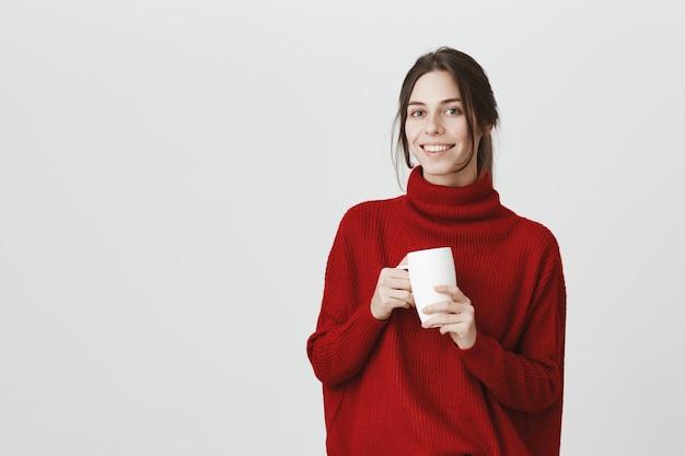 Young female employee drinking coffee, holding mug and smiling