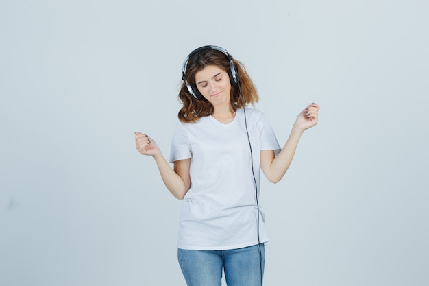 Free Photo young female enjoying music with headphones in white t-shirt, jeans and looking frisky. front view.