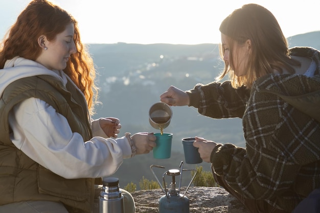 Free photo young female friends drinking hot tea in mountains