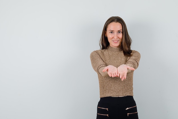 Free photo young female in golden blouse posing like holding something on hands and looking pleased , front view. space for text