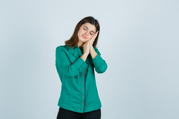 Young female in green shirt leaning on palms as pillow and looking peaceful , front view.