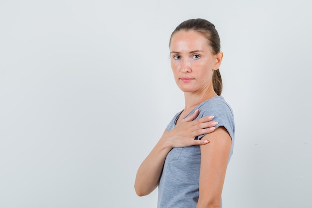 Free Photo young female in grey t-shirt holding hand near heart and looking serious , front view.