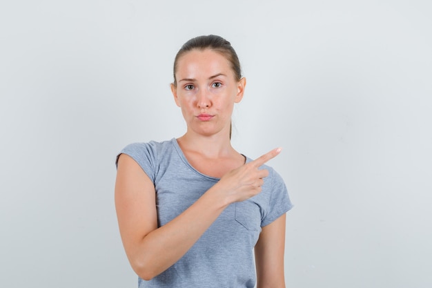 Young female in grey t-shirt pointing to side and looking serious , front view.