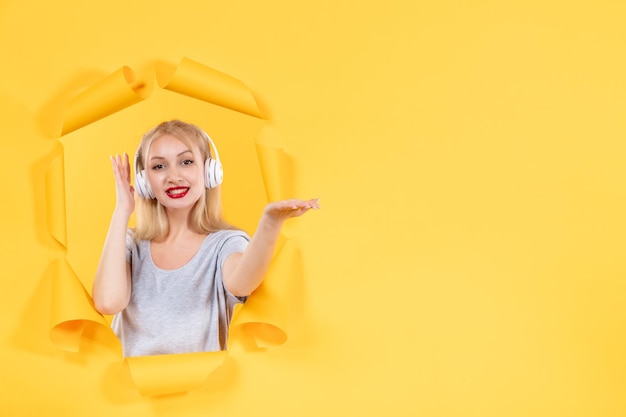 Young female in headphones pointing at something on yellow background audio sounds ultrasound