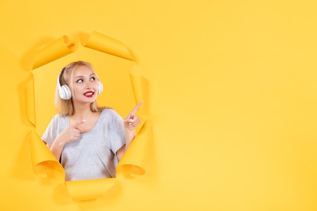 Young female in headphones on the torn yellow paper background audio ultrasound music sound