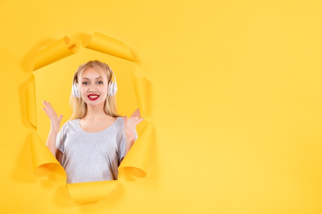 Free photo young female in headphones on the torn yellow paper background ultrasound music audio sound