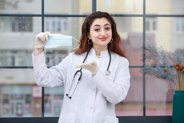 A young female health care worker holding mask and showing it with hand