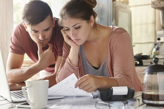 Young female and her unemployed husband with many debts doing paperwork together in kitchen